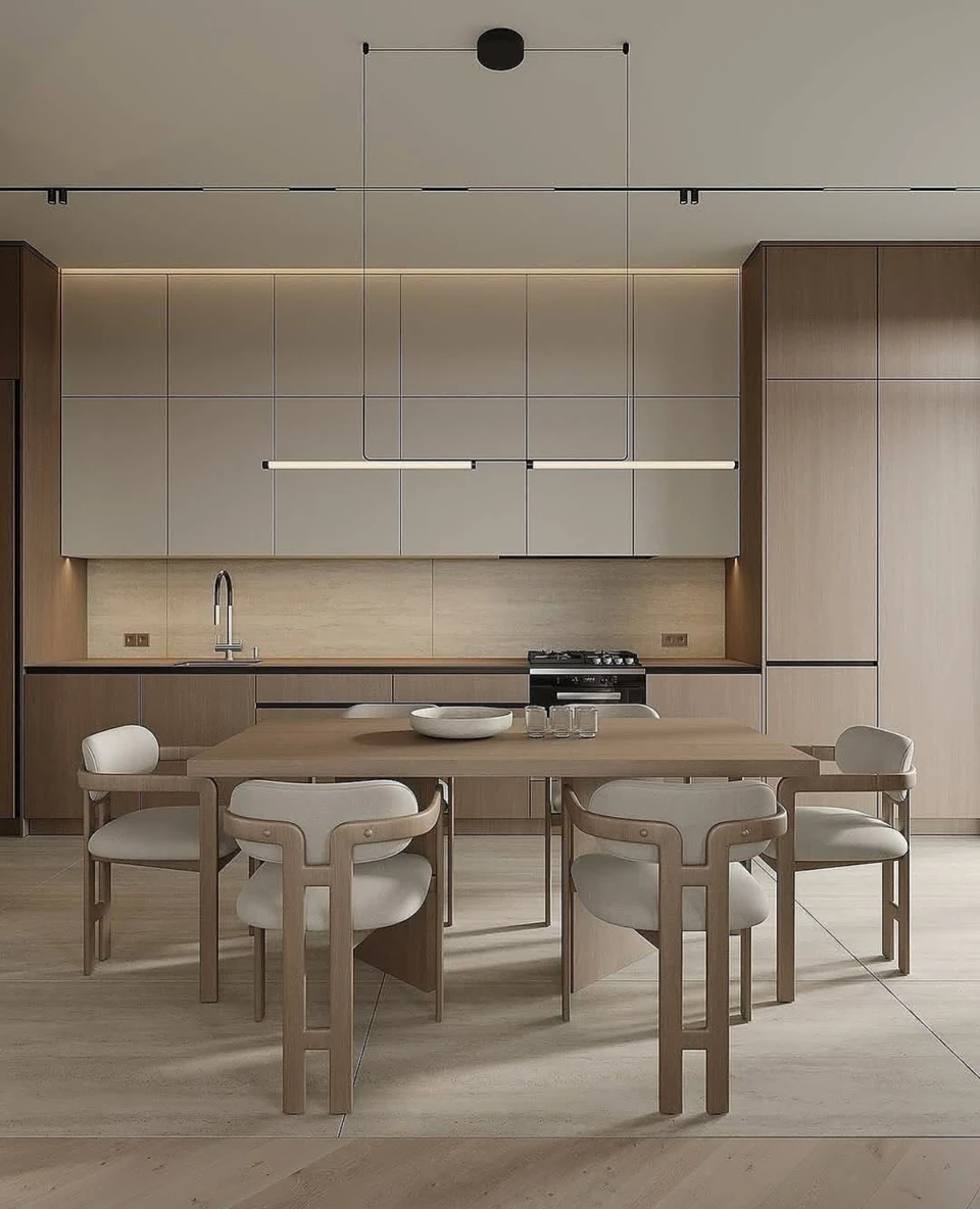 A rectangular wood-toned dining table and upholstered chairs face a coordinated wall of pale kitchen cabinetry.