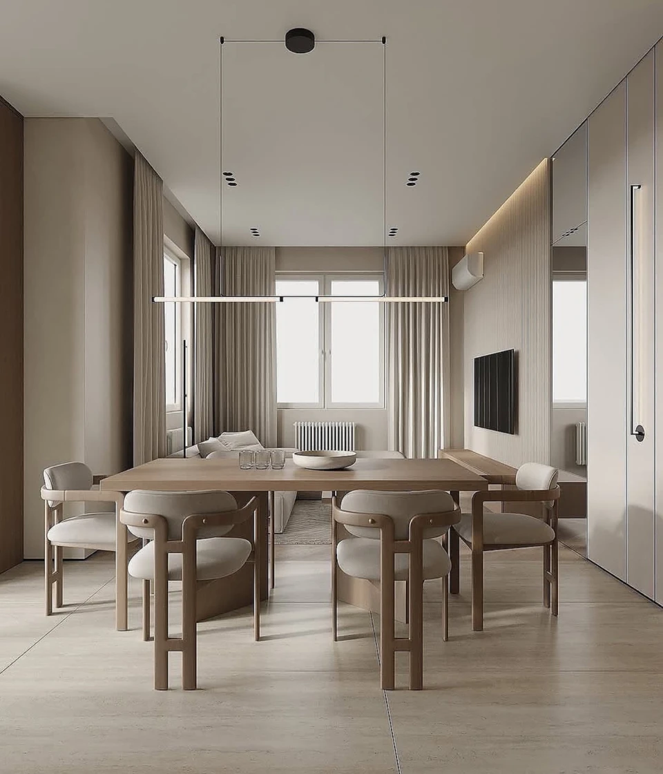 Kitchen, dining and living zones share warm neutral tones and slender suspended lighting.